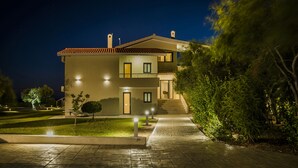 Una casa de dos pisos con techo de tejas, una entrada bien iluminada y un camino de entrada pavimentado que lleva a la puerta principal.