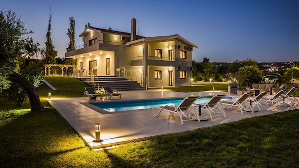 Una casa moderna de dos pisos con piscina, mobiliario exterior y un patio bien iluminado.