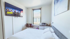 A bedroom with a bed, a TV mounted on the wall, a window, and a desk with a chair. - City Studio | Netflix Premium 4K | 65" LG QLED TV | Queen Memory Foam Bed (Adelaide)