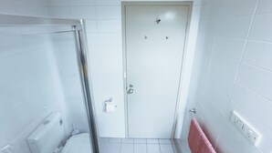A bathroom with white tiled walls, a white door, a glass shower enclosure, a toilet, and a pink towel hanging on the wall. - City Studio | Netflix Premium 4K | 65" LG QLED TV | Queen Memory Foam Bed (Adelaide)