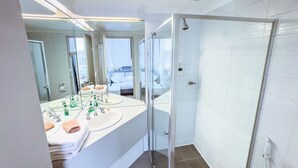 A modern bathroom with a glass-enclosed shower, dual sinks, and a large mirror. - City Studio | Netflix Premium 4K | 65" LG QLED TV | Queen Memory Foam Bed (Adelaide)