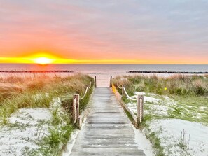 A wooden boardwalk leading to a beach with a sunset in the background. - Pelican Home with Rooftop Deck & Walk to Beach (Cape Charles)