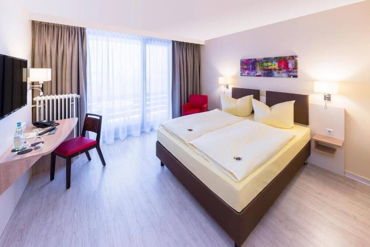 A hotel room with a large bed, a desk with a chair, a television, and a window with curtains.