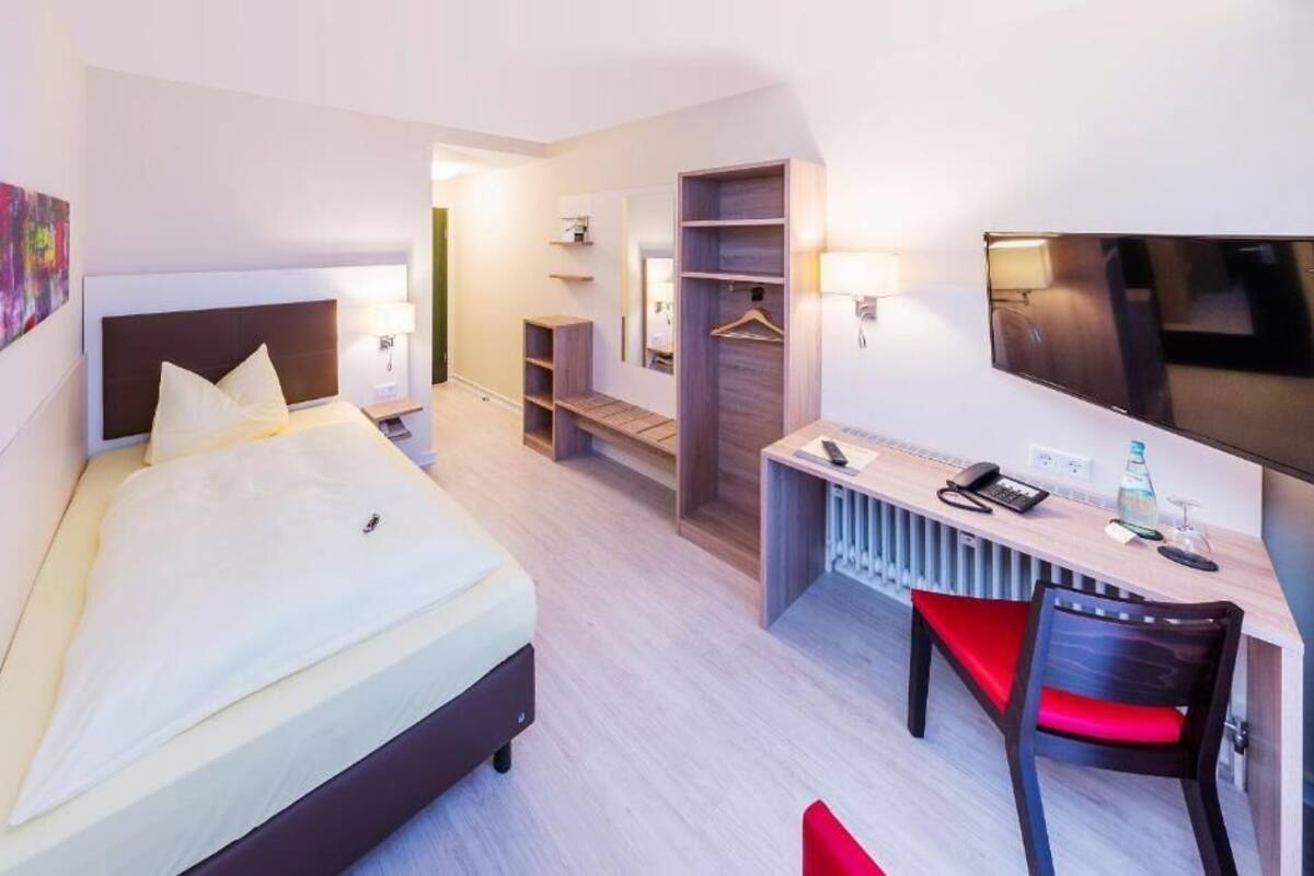 A hotel room with a bed, a desk with a chair, a TV, and a walk-in closet.