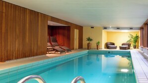 An indoor swimming pool with lounge chairs and potted plants.