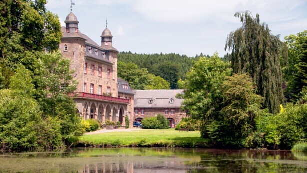 A historic building with a large courtyard and a pond in front.
