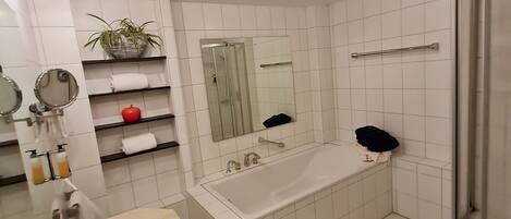 Un baño moderno con una bañera grande, zona de ducha y tocador con espejo y lavamanos.