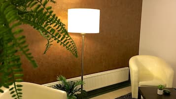 Ein Zimmer mit einem weißen Sessel, einer Stehlampe, einem kleinen Tisch mit einer Pflanze und einem großen Farn.
