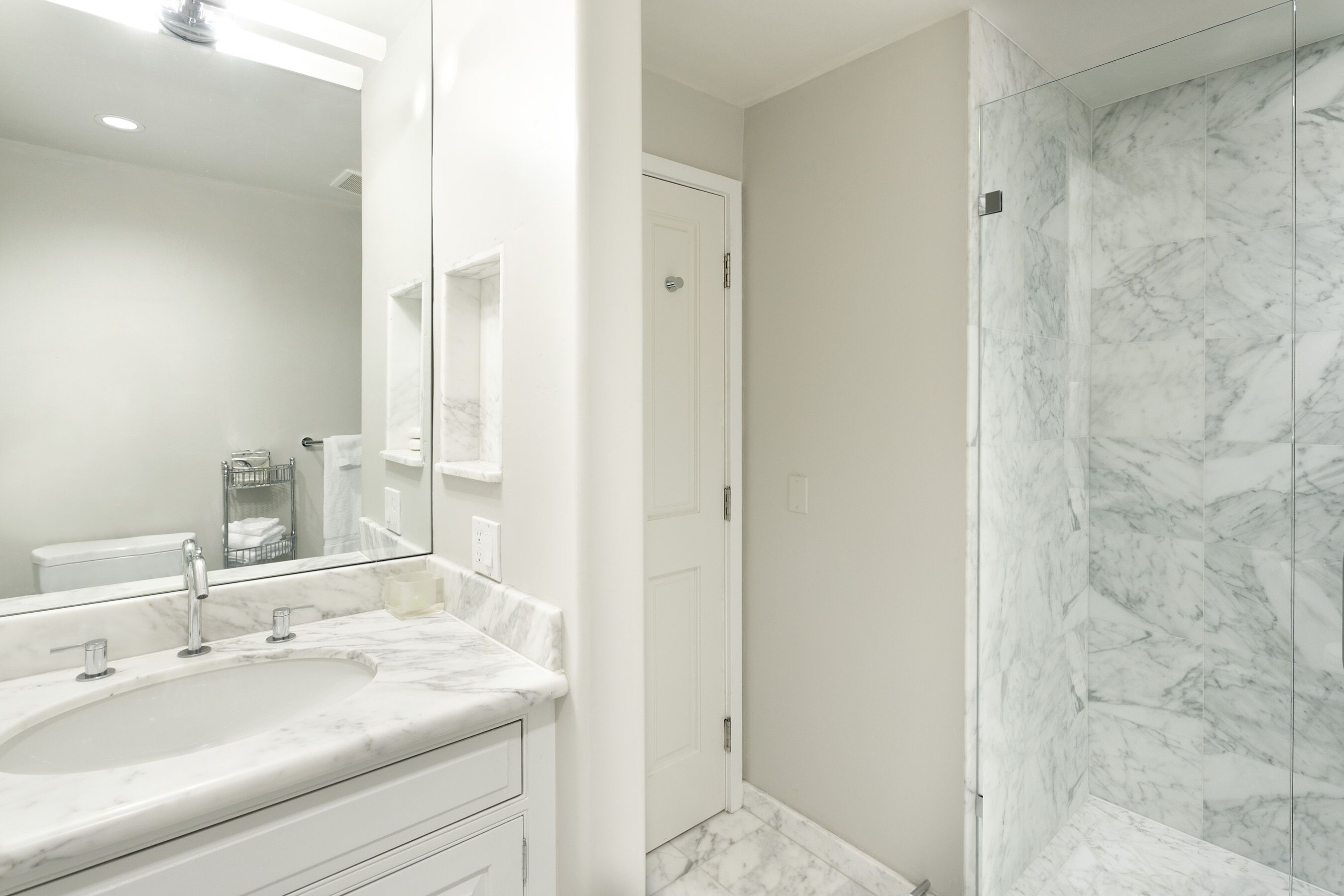 A modern bathroom with a marble sink, a large mirror, and a glass shower enclosure.