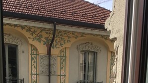 Ein Balkon mit Metallgeländer, der auf ein Gebäude mit aufwendigen architektonischen Details und Fensterläden blickt.