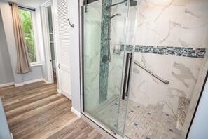 A modern bathroom with a glass-enclosed shower, a tiled floor, and a window with curtains.