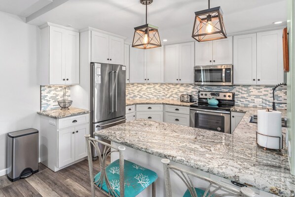 A modern kitchen with white cabinets, a granite countertop, stainless steel appliances, and a unique backsplash.