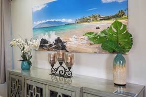 A room with a beach scene painting, a vase with white flowers, and a decorative candle holder.