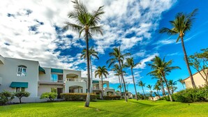 A resort with a well-maintained lawn, palm trees, and a modern building with multiple balconies. - Palms at Wailea #803 Fully Renovated, Partial Ocean View! Free Wifi, Full A/C (Wailea)