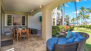 A covered outdoor area with a dining table and chairs, a wicker sofa with cushions, and a view of a landscaped garden with palm trees. - Palms at Wailea #803 Fully Renovated, Partial Ocean View! Free Wifi, Full A/C (Wailea)
