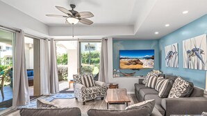 A modern living room with a sofa, armchairs, and a coffee table. There is a ceiling fan, a large window with curtains, and artwork on the wall. - Palms at Wailea #803 Fully Renovated, Partial Ocean View! Free Wifi, Full A/C (Wailea)