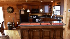 A wooden cabin interior with a kitchen featuring a central island with bar stools, a microwave, and a refrigerator. - Gatlinburg Luxury Cabin, 4 Master Bdrms, Theater, Game Rm, Hot Tub, Perfect! (Sevierville)