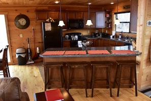 Interno di una baita in legno con cucina, caratterizzata da un'isola centrale con sgabelli da bar, un forno a microonde e un frigorifero.