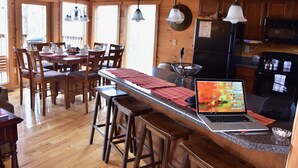 A wooden interior with a kitchen area, dining table, bar stools, and a laptop on the counter. - Gatlinburg Luxury Cabin, 4 Master Bdrms, Theater, Game Rm, Hot Tub, Perfect! (Sevierville)
