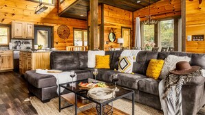 Ein gemütliches Blockhaus-Interieur mit Wohnbereich, der ein Ledersofa, einen Couchtisch und eine Küchenzeile mit Holzschränken und einer Arbeitsplatte umfasst.