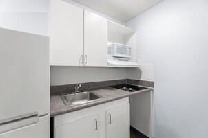 Una cocina con gabinetes blancos, encimera de granito, pileta de acero inoxidable y microondas.