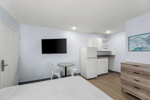 Una habitación compacta con cama, una pequeña mesa de comedor con sillas, kitchenette, televisor de pantalla plana y cómoda de madera.