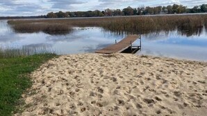A sandy beach with a wooden dock extending into calm water, surrounded by trees and a partly cloudy sky.