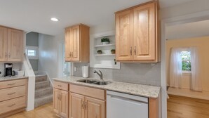 A kitchen with wooden cabinets, a sink, and a countertop. There is a staircase leading to another level.