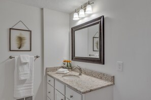 Une salle de bain équipée d’un lavabo, d’un miroir, d’un porte-serviettes et d’œuvres d’art encadrées.