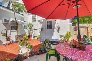 Eine Terrasse mit einem roten Sonnenschirm, grünen Stühlen und Topfpflanzen.