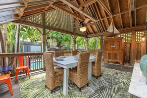 An outdoor dining area with wicker chairs, a table, and a pool in the background.