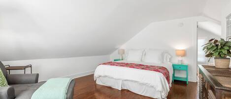 A bedroom with a bed, a chair, a nightstand, a dresser, and a potted plant.