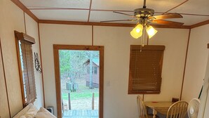 A bedroom with a bed, a ceiling fan, a window, a door, and a small table with chairs. - Fenced for your fur babies! 2 cabins on property for 1 price! (Mena)