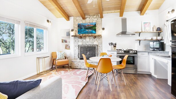 Una cucina moderna con camino in pietra, travi a vista in legno e zona pranzo con sedie arancioni.