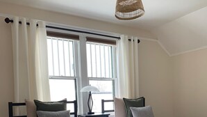 A bedroom with two beds, a large window, a hanging light fixture, and a patterned rug.