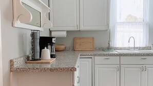 A kitchen with white cabinets, a granite countertop, a coffee maker, a cutting board, and a window with a sink.