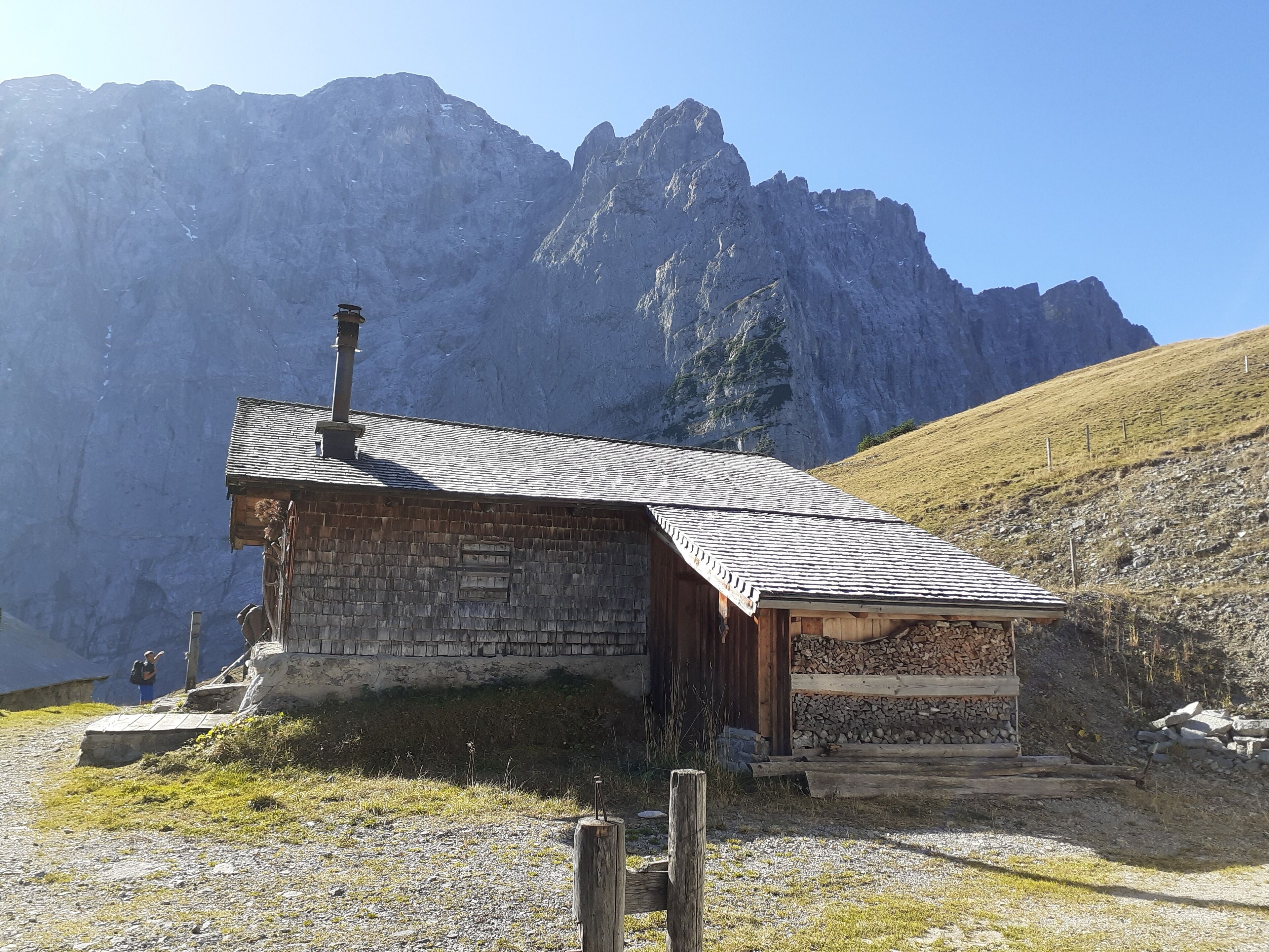 Un chalet de montagne rustique, avec une façade en pierre et un toit en bois, situé dans une région montagneuse sous un ciel dégagé.