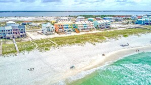 A coastal area with colorful buildings, a sandy beach, and a view of the ocean. - A Bitter Acorn: Newly Built, Gulf Front Home | Navarre Beach (Navarre Beach)