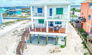 A two-story beachfront house with a wooden deck and outdoor seating area.