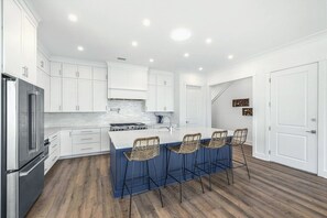 A modern kitchen with white cabinets, a stainless steel refrigerator, a built-in stove, and a large island with bar stools.