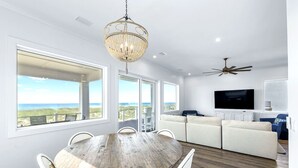 A spacious living area with a large wooden dining table, white sofas, and a TV. - A Bitter Acorn: Newly Built, Gulf Front Home | Navarre Beach (Navarre Beach)