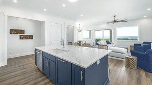 A spacious kitchen with a large island, white walls, and a view of the ocean. - A Bitter Acorn: Newly Built, Gulf Front Home | Navarre Beach (Navarre Beach)