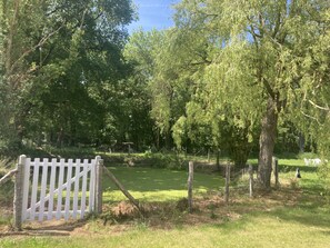 A fenced area with a white gate, trees, and a grassy field.