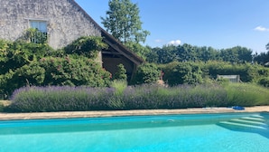 En swimmingpool med kristallklart blått vatten, omgiven av frodig gr önska och en byggnad av sten med ett litet fönster.