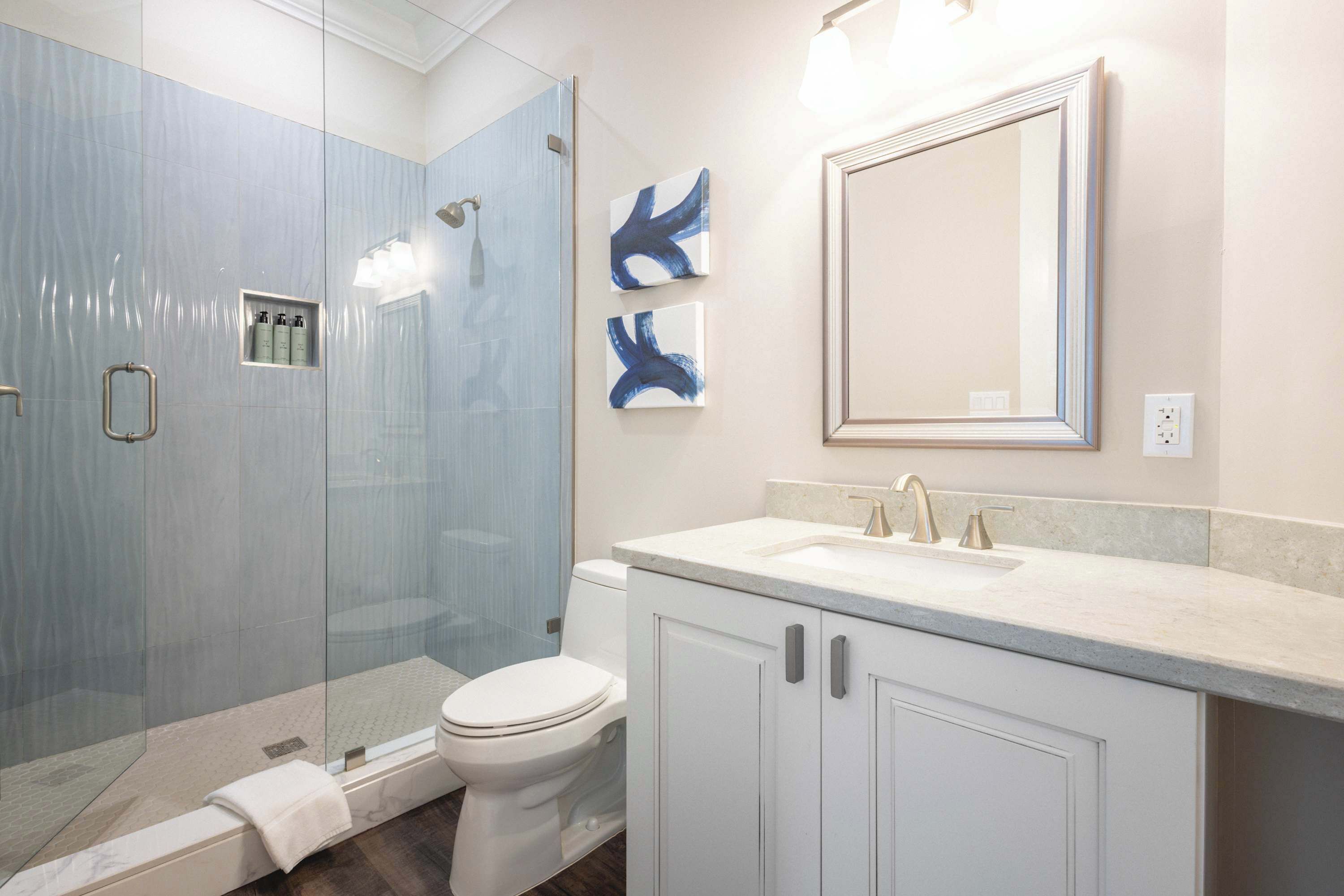 Un bany modern amb un espai de banyera de vidre, un vàter blanc i un lavabo amb un rentapelums i un mirall.