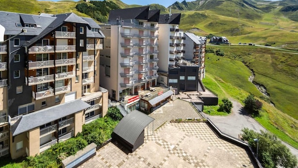 Ein mehrstöckiges Hotel mit Balkonen, einer Terrasse und Blick auf grüne Hügel.