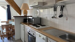 Eine kleine Küche mit Mikrowelle, Herd und Geschirrspüler. Ein Holztisch mit Stühlen und einer Lampe steht bereit.