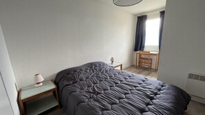 Ein Schlafzimmer mit einem großen Bett, einem Nachttisch mit Lampe, einem Sessel und einem Fenster mit Vorhängen.
