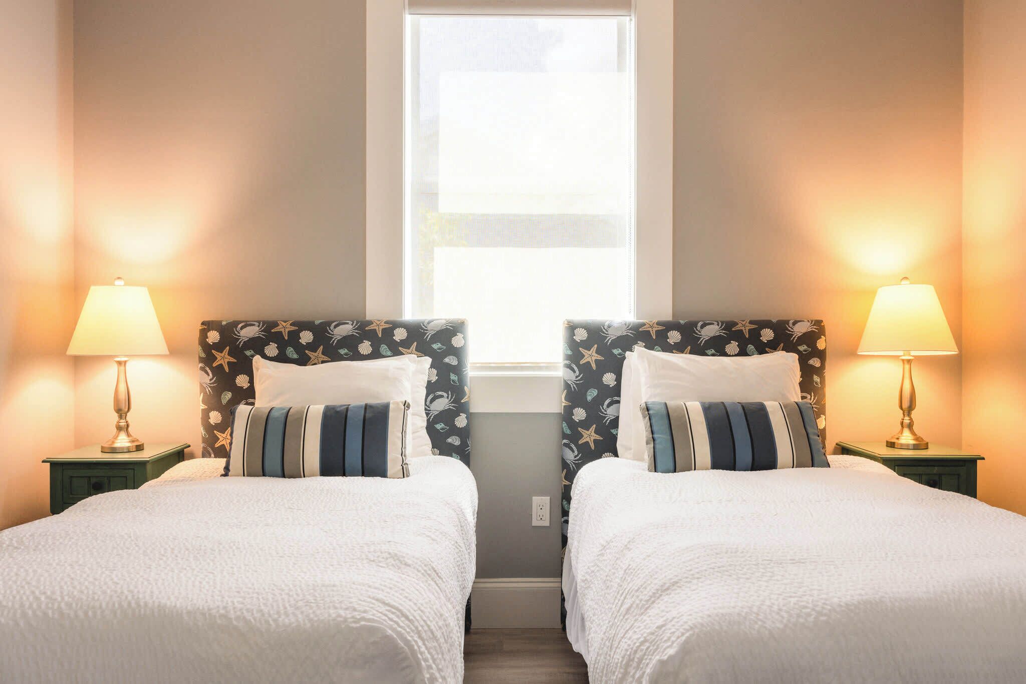 Habitación doble con dos camas, cada una con cabecero decorado con motivos de estrellas. Hay lámparas de noche sobre mesitas a juego, y una ventana sobre las camas.