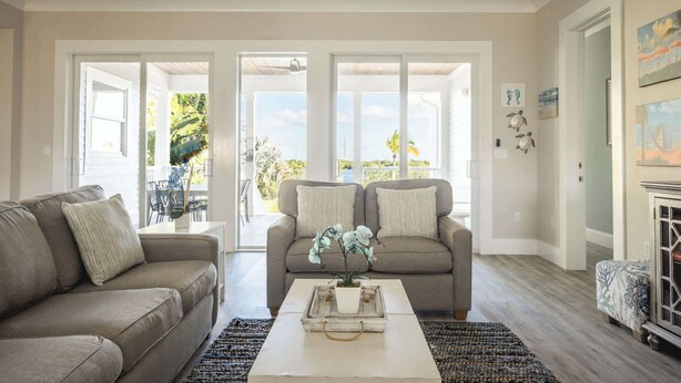 A living room with a beige sofa, a white coffee table with a plant, and a view through glass doors to an outdoor area. - Waterlane House at Lunara Bay (Key West)